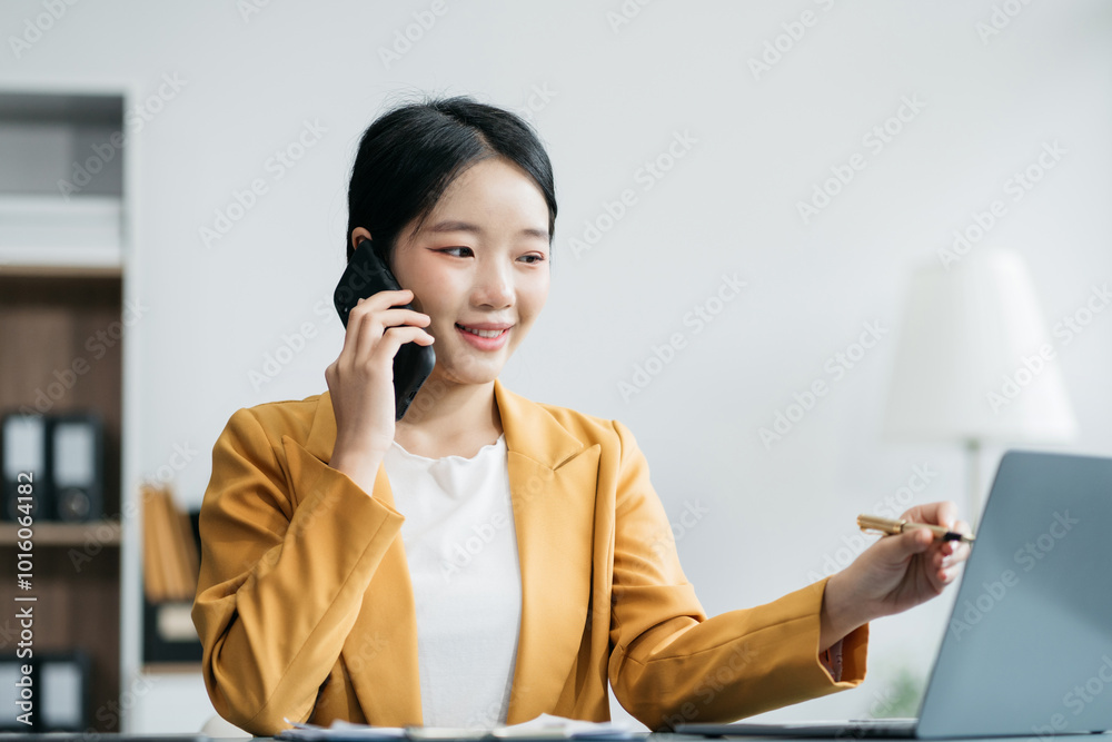 Asian businesswoman talking mobile phone and working on laptop and papers on table in her office. Asian businesswoman talking mobile phone and working on laptop and papers on table in her office.