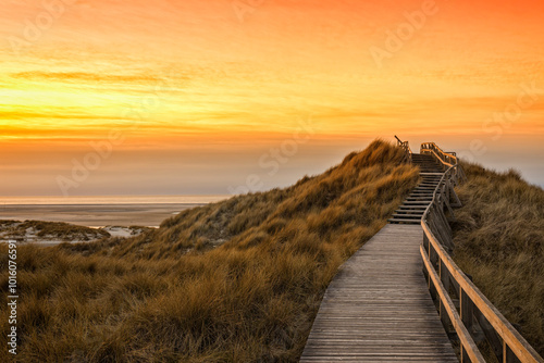 Fototapeta Naklejka Na Ścianę i Meble -  Wooden path and stairs crossing the dunes to the beach of Norddorf, Amrum, in sunset