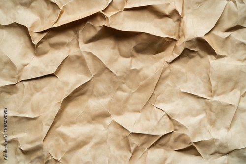 Close-up of a crumpled brown paper texture. The surface showcases various folds, creases, and wrinkles, creating an abstract and rustic background.