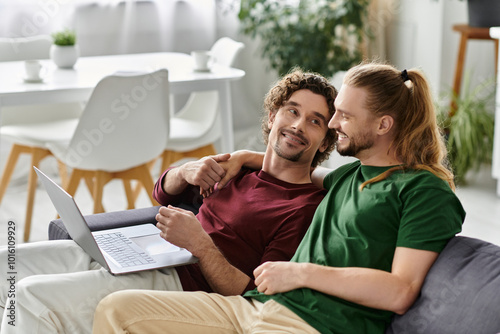 A handsome couple cuddles on the couch while sharing a laptop.