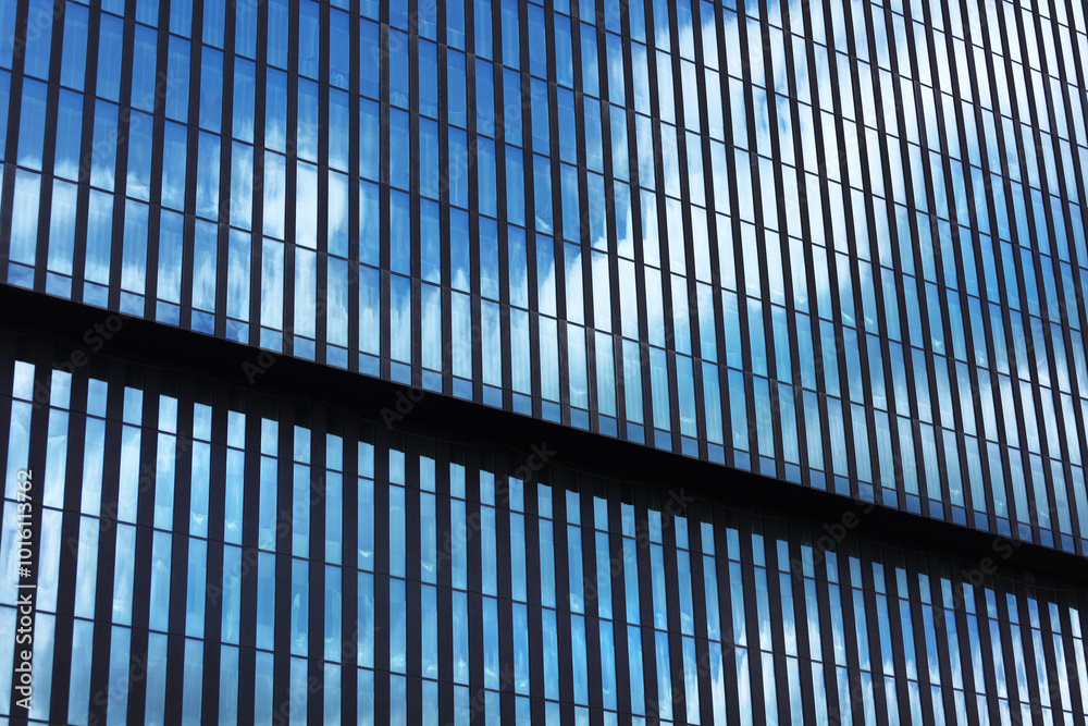 Perspective view office building facade, sky reflections in windows. Modern skyscraper made of blue toned glass and steel constructions under blue sky. Horizontal photo with place for text.
