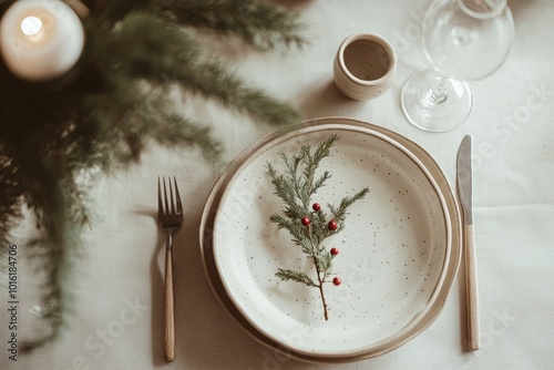 A close-up of a rustic table setting featuring a white plate adorned with evergreen branches and red berries, offering a simple yet elegant holiday decoration idea. photo