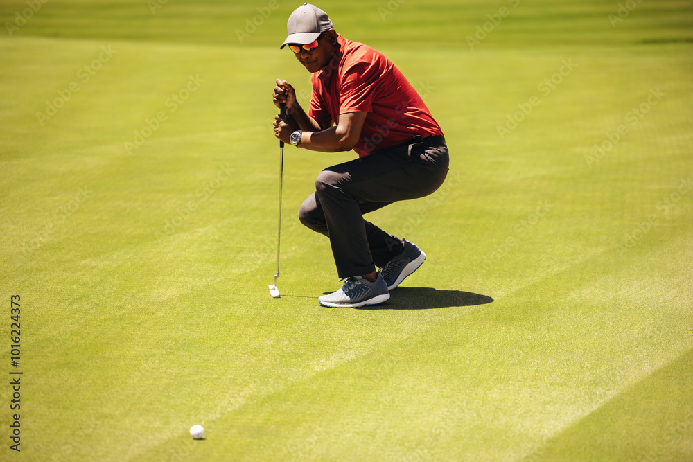 Obraz premium Focused golfer aiming carefully while leaning on putter to line up a crucial shot on the green