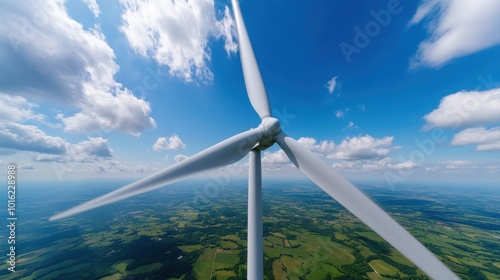 A picturesque view of a wind turbine spinning amidst vast fields below, showcasing the harmony of technology with nature under a clear blue sky filled with clouds.