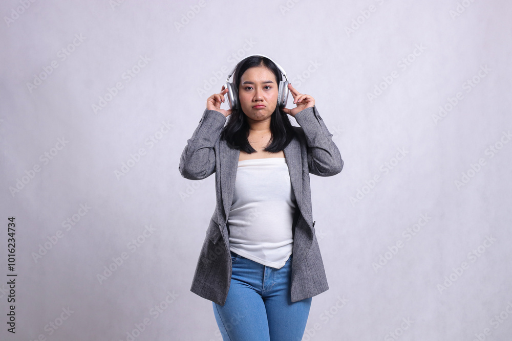 beautiful young office ladies pouting holding and wearing headphone headset listening music wearing grey suit isolated on white background. lifestyle, advertising, entertainment, technology concept beautiful young office ladies pouting holding and wearing headphone headset listening music wearing grey suit isolated on white background. lifestyle, advertising, entertainment, technology concept