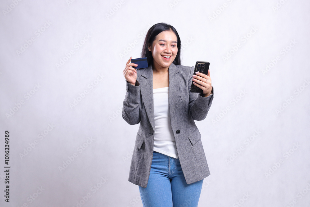 Beautiful young office lady asia cheerful candid hold mobile phone smartphone and hold credit debit member card wearing gray suit isolated on white background. for finance, transaction content Beautiful young office lady asia cheerful candid hold mobile phone smartphone and hold credit debit member card wearing gray suit isolated on white background. for finance, transaction content