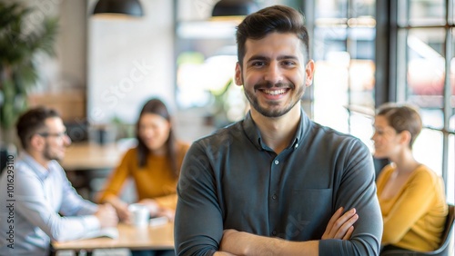 Confident young man smiling with arms crossed in a relaxed office atmosphere.