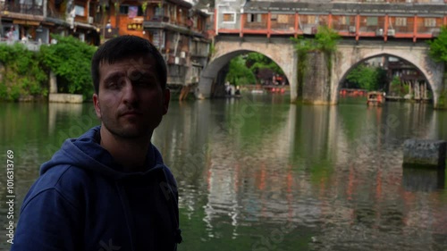 Tourist man watching the scenery near Rainbow Bridge in Tuojiang River. Fenghuang, China photo