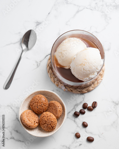 Affogato coffee with vanilla ice cream scoops and espresso in a glass on a marble background with coffee beans and cookies.