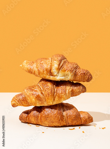 Stack of fresh croissants on yellow and orange background. Creative trendy layout and concept of healthy food or french breakfast. Copy space.