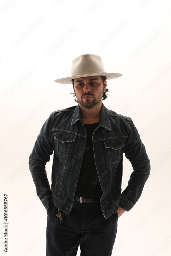 Portrait of bearded handsome man wearing denim jacket and fedora hat looking at the camera. Vertical. Portrait of bearded handsome man wearing denim jacket and fedora hat looking at the camera. Vertical.