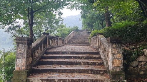 Stone steps leading up a hill through lush green foliage with a view of a misty mountain peak in the distance.