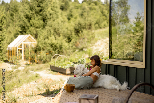 Obraz na płótnie A serene scene where a woman and her loyal dog relax on the porch, taking in the beauty of the natural landscape. The reflection in the glass adds depth to the composition w salonie