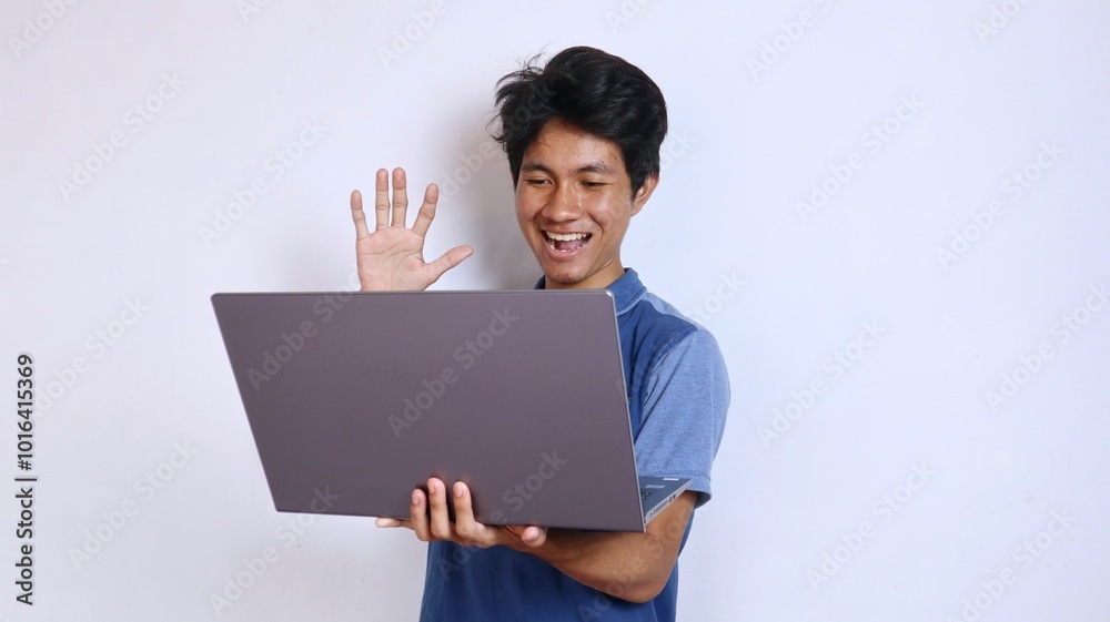 Asian young man smiling gesture holding and looking at laptop say hi Asian young man smiling gesture holding and looking at laptop say hi