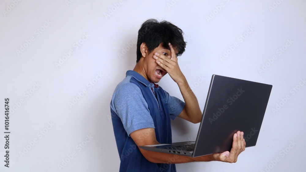 shocked asian male youth holding laptop gesture closing eyes looking and peeking at laptop shocked asian male youth holding laptop gesture closing eyes looking and peeking at laptop