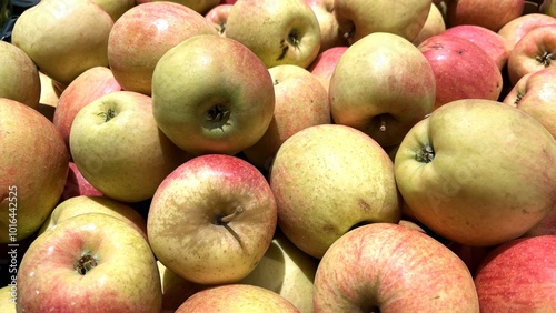 A close-up photo of a pile of apples, primarily green with varying shades of red blush. Fresh and crisp, with visible stems and a slight sheen apples