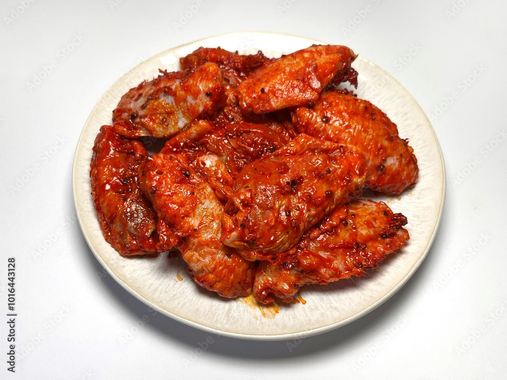 Marinated spicy chicken wings on a plate on a white background, isolated. Top view. Copy space. Semifinished. Fast cooking. Raw marinated chicken meat. Marinated spicy chicken wings on a plate on a white background, isolated. Top view. Copy space. Semifinished. Fast cooking. Raw marinated chicken meat.
