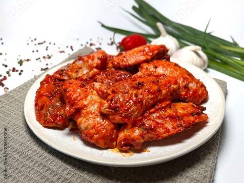 Raw marinated spicy chicken wings on a plate with spices and vegetables on a white background.  Fast cooking. Raw marinated chicken meat.