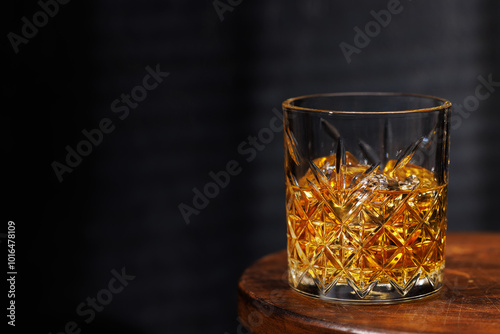 A whiskey glass resting on a wooden table, set against a dark background