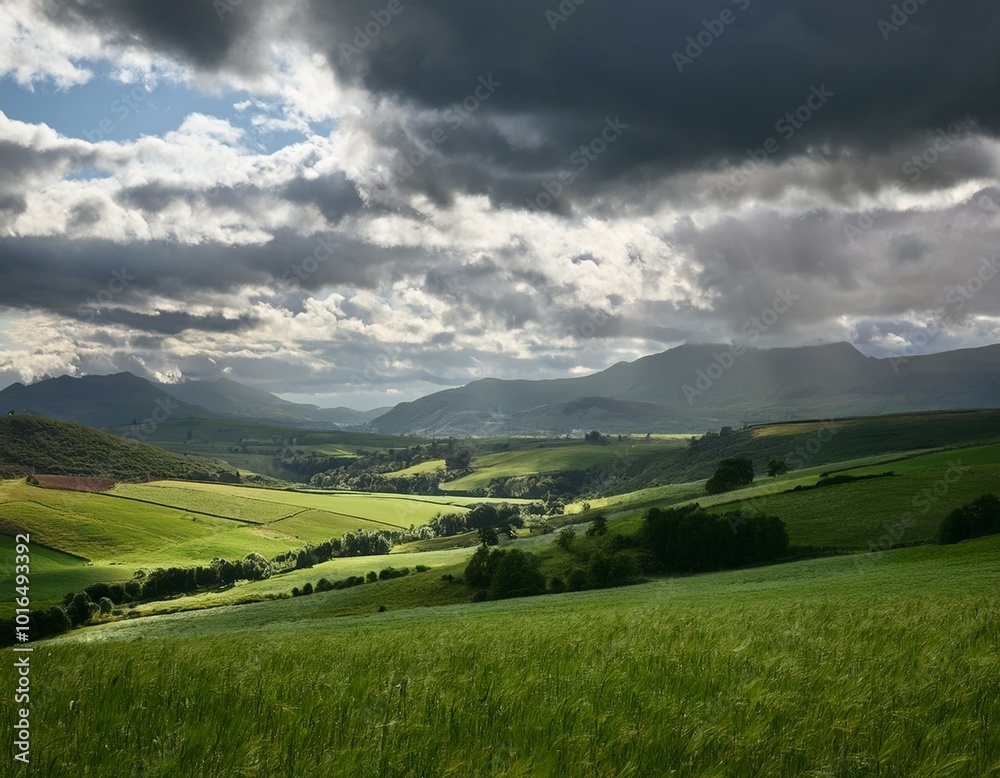 Obraz premium The dramatic sky above the distant valley adds a touch of mystique, while the green fields ground the scene in tranquil reality.