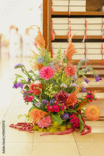 Vibrant flower arrangement placed beside stacked hymn books in a bright indoor space, likely a church or ceremonial setting.