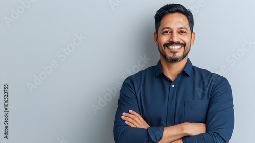 charismatic indian businessman in smart casual attire confident pose with folded hands against clean white backdrop warm smile conveys approachability and professionalism modern corporate portrait photo