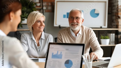 Smiling business team in a meeting, discussing graphs and charts on laptops in a modern office setting, showcasing teamwork and collaboration.