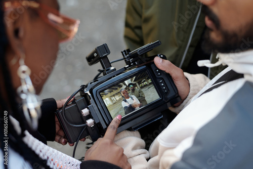 People examining footage on professional camera screen during outdoor shoot. Focus on digital display showing captured scene with engaged participants