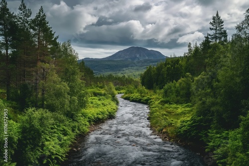 Serene landscape with winding river, rocky bed. Green vegetation surrounds river with dense forest, tall trees. Majestic mountain range in distance with peaks obscured by cloudy sky. Harmonious,