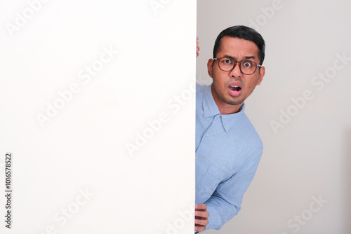 A man peeking behind wall seeing something with confused expression photo