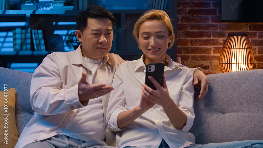 Diversity family multiracial couple Asian man Caucasian woman shopping online with smartphone mobile phone app choose goods store buying emotional discuss order food delivery night evening home couch Diversity family multiracial couple Asian man Caucasian woman shopping online with smartphone mobile phone app choose goods store buying emotional discuss order food delivery night evening home couch