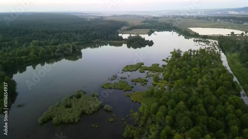 Aerial view of a natural landscape near a mountain town with a dense green forest, several small lakes or ponds, valleys and mountains in some places shrouded in fog