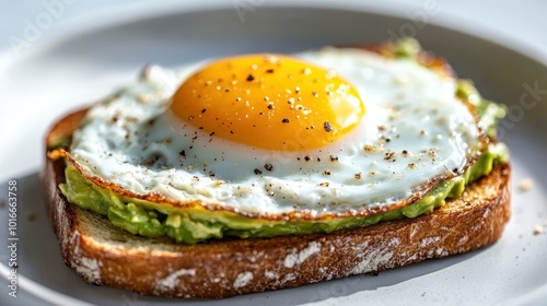 A close-up shot of a delectable avocado toast topped with a perfectly cooked sunny-side-up egg, seasoned with pepper, showcasing a modern and healthy breakfast choice.