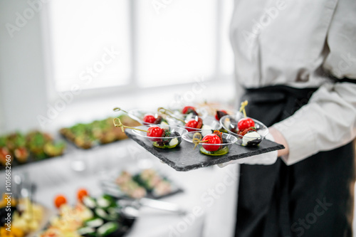 Foto A waiter in a white shirt and black apron holds a tray of appetizers with cherry tomatoes and mozzarella at a catered event