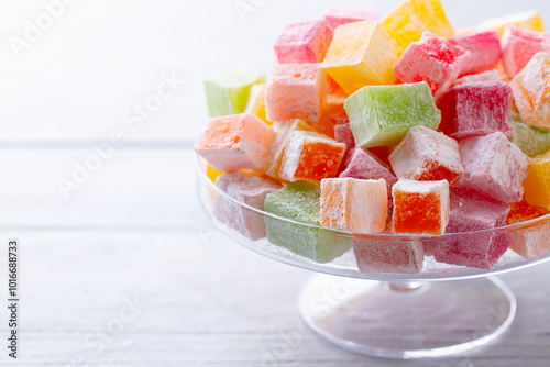 Turkish delights on glass cake stand, bowl with rose flowers. White background Close up. Copy space.