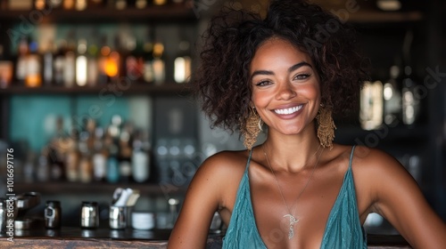 A joyful woman with curly hair beams a warm smile in a stylish bar setting, exuding confidence and charisma amid a lively backdrop of bottles and ambient lighting.