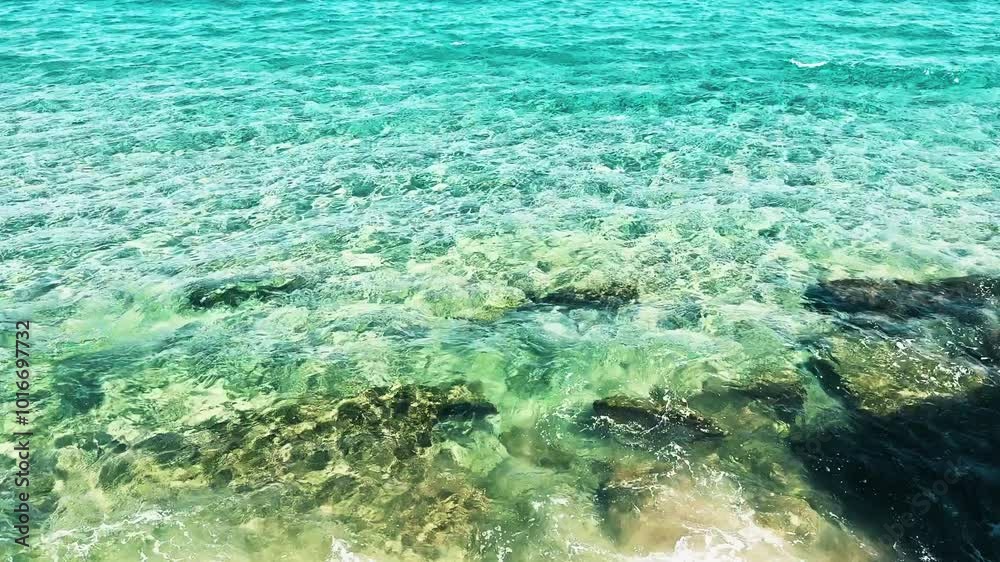 The ocean is calm and clear, with a few rocks visible in the water. Scene is peaceful and serene, as the water appears to be still and undisturbed
