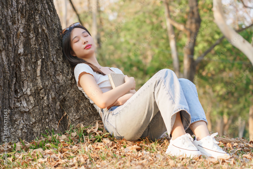 Young asian women sitting on grass and to leaning the tree and sleeping with dreaming to resting after reading a literature book while relaxation with journey travel lifestyle in the nature park Young asian women sitting on grass and to leaning the tree and sleeping with dreaming to resting after reading a literature book while relaxation with journey travel lifestyle in the nature park