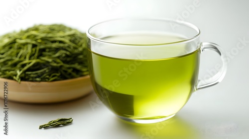 A clear glass cup filled with fresh green tea sits beside a bowl of loose green tea leaves, showcasing a soothing, herbal aesthetic.