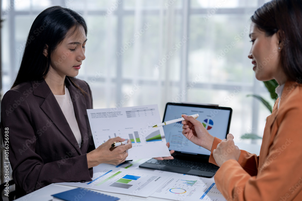Two businesswomen are discussing a financial project and analyzing graphs on a laptop Two businesswomen are discussing a financial project and analyzing graphs on a laptop