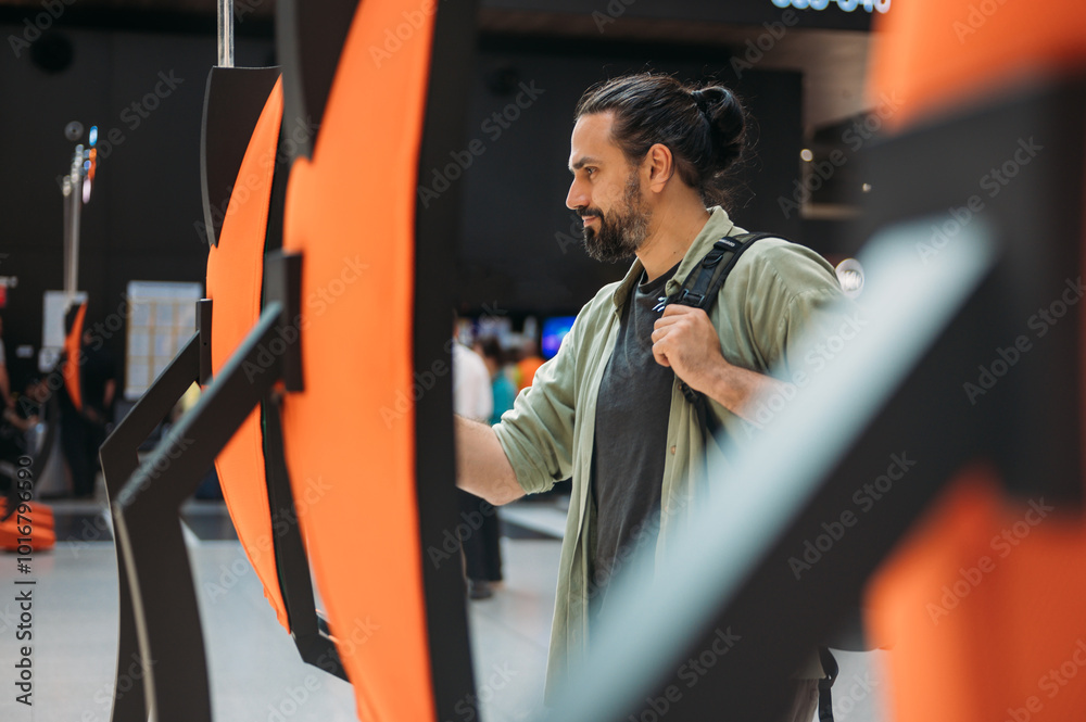 Naklejka premium A man checks in for a plane at the electronic check-in desk. A young tourist guy at the airport gets a ticket at the check-in screen