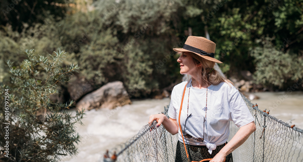 A young woman on a pedestrian suspension bridge on a vacation trip. A happy girl in a hat takes photos of a sunny landscape on a bridge in the mountains A young woman on a pedestrian suspension bridge on a vacation trip. A happy girl in a hat takes photos of a sunny landscape on a bridge in the mountains
