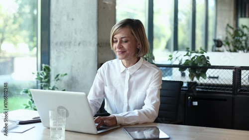 Attractive middle aged woman working at office, using contemporary desktop laptop photo