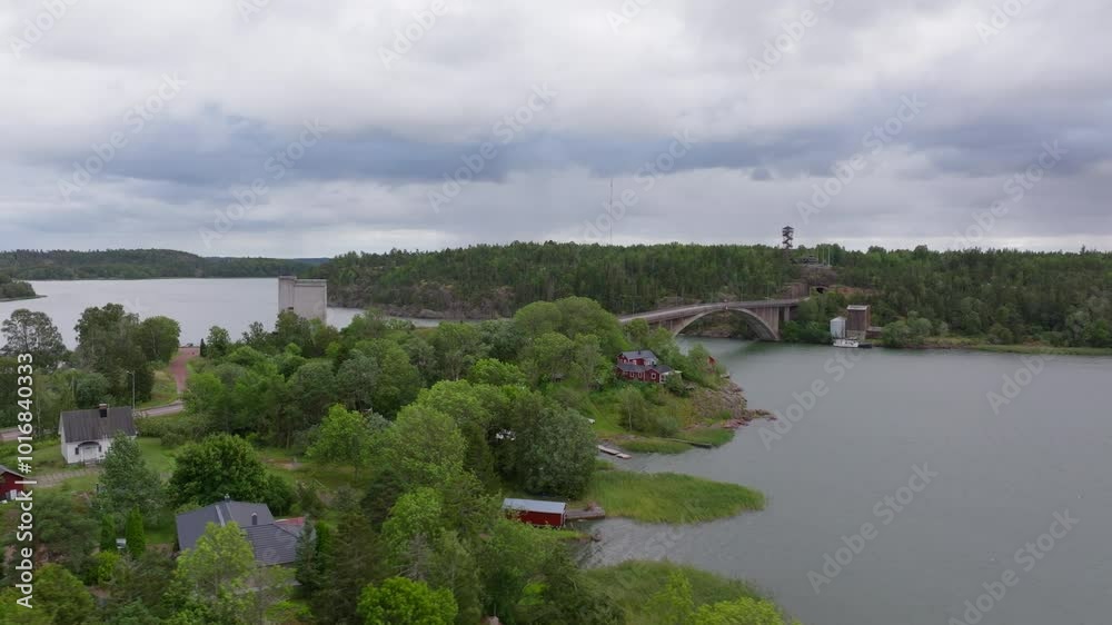 Aerial views highlight a bridge linking small islands in Aland, Finland. Calm waters mirror the overcast sky, while quaint houses enhance the tranquil landscape Aerial views highlight a bridge linking small islands in Aland, Finland. Calm waters mirror the overcast sky, while quaint houses enhance the tranquil landscape