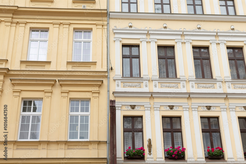 There are two charming buildings situated closely side by side, each adorned with beautiful flowers blooming in their windows There are two charming buildings situated closely side by side, each adorned with beautiful flowers blooming in their windows