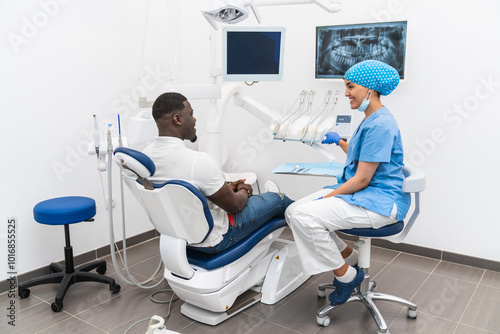 Dental hygienist smiling while preparing tools during a dental checkup with an African male patient.