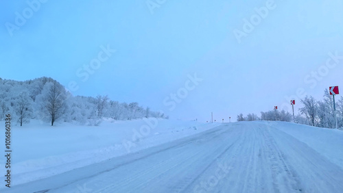 A serene, snow-covered rural road under a clear blue sky, representing winter travel challenges and the beauty of remote seasonal landscapes