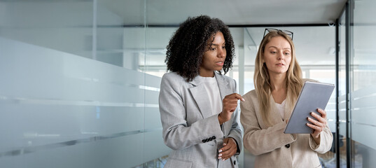 Two businesswoman working together using digital work tablet pc business project. Small creative diversity team of African American female and young woman do meeting in office. Banner, copy space