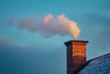 Brick chimney releasing smoke against blue sky in winter