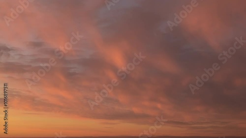 Time lapse. Sunset sky with soft, fluffy, pastel colored clouds moving on pink, orange, burgundy sky